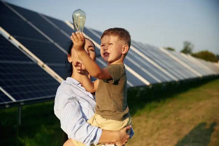 Taking a look at the light bulb. Mother with her little son are near the solar panels.
